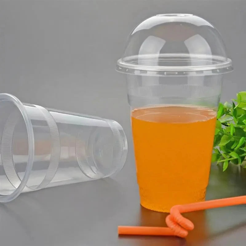 A clear plastic cup with a dome lid filled with orange juice, next to another empty cup and an orange straw.