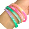 A hand is wearing a stack of silicone bracelets with the word Jesus engraved on them in various pastel colors.
