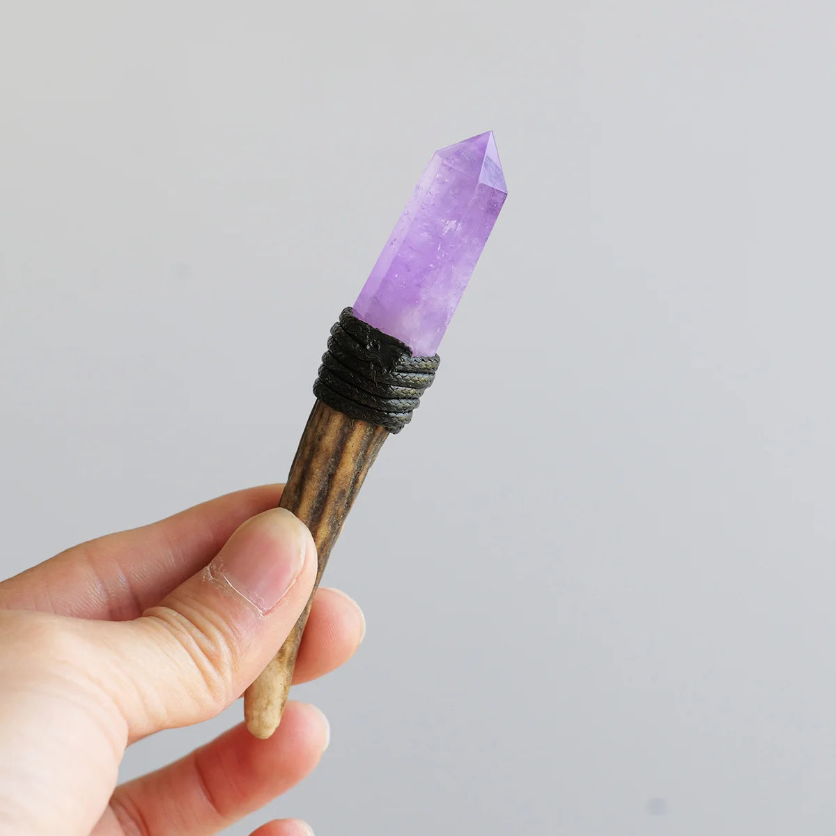 A hand holds a natural crystalHerkimer scepter wand with a purple point and dark wrapping for spiritual decor.