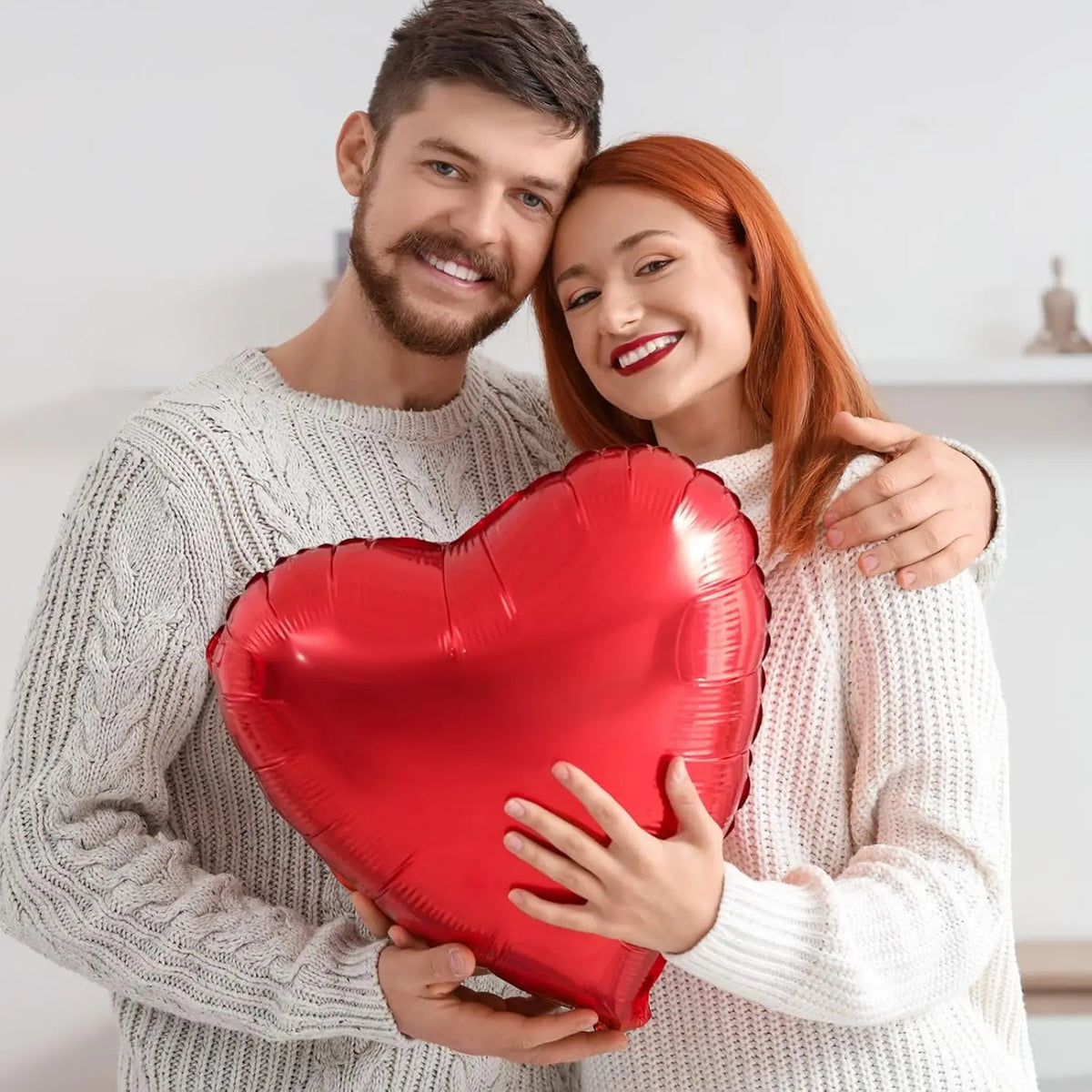 A couple holding a red heart foil balloon for Valentine's Day or wedding decorations.