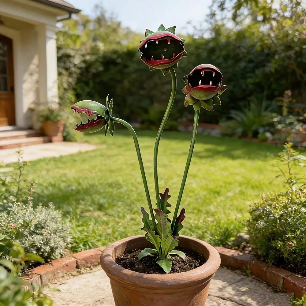 A decorative metal carnivorous flower garden stake with three flower heads growing in a terracotta pot.