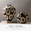 Two black and beige ceramic vases with geometric circle designs on a light gray background.