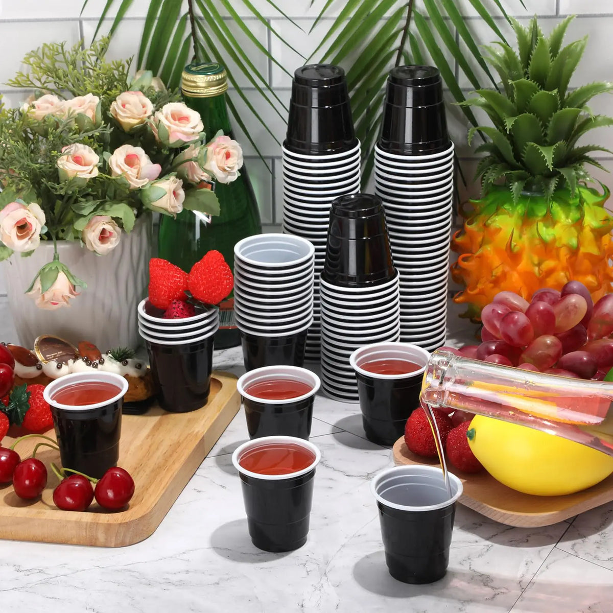 A collection of mini plastic shot cups in black and white stripes arranged on a wooden board with fresh fruit.