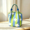 A light blue and lime green striped knitted shoulder bag with a blue patterned strap sits on a wooden surface.
