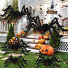 Giant black plush spider decoration hanging in front of a white door with Halloween decor.