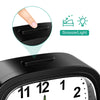 A close-up view of a black analog alarm clock with a luminous display and snooze function.