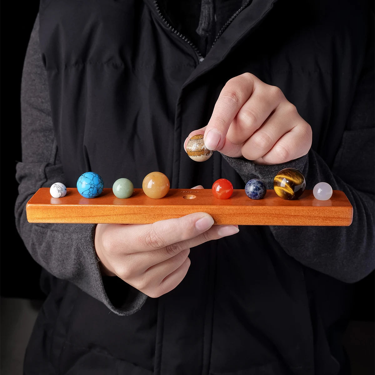 A hand holds a set of natural crystal solar system planet balls on a wooden board.