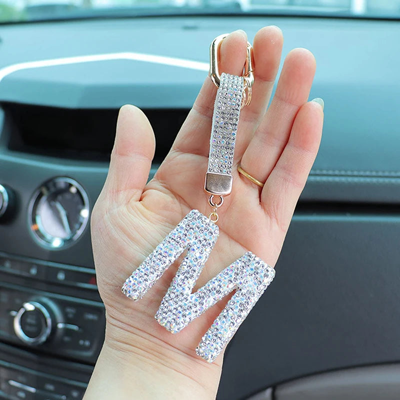 A hand holds a silver letter keychain charm with a sparkling crystal design.