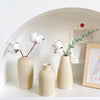 Three minimalist ceramic vases in beige tones displayed on a white shelf with a framed card.