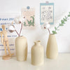 A collection of minimalist ceramic vases and a wooden figure displayed on a white surface with botanical cards.