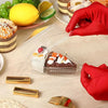 Eine Hand in roter Handschuh hält eine klare Plastik-Lebensmittelschachtel mit einem Dessert.