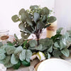 A bouquet of artificial eucalyptus stems with silvery-green leaves and small white flowers displayed on a table.