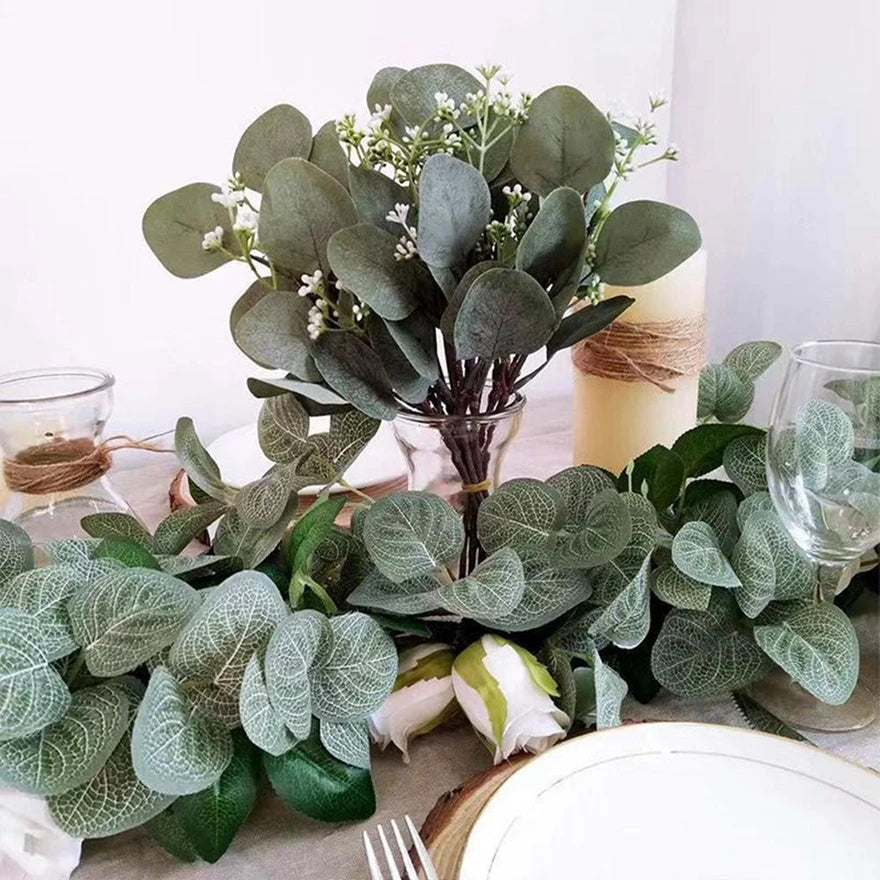 A bouquet of artificial eucalyptus stems with silvery-green leaves and small white flowers displayed on a table.