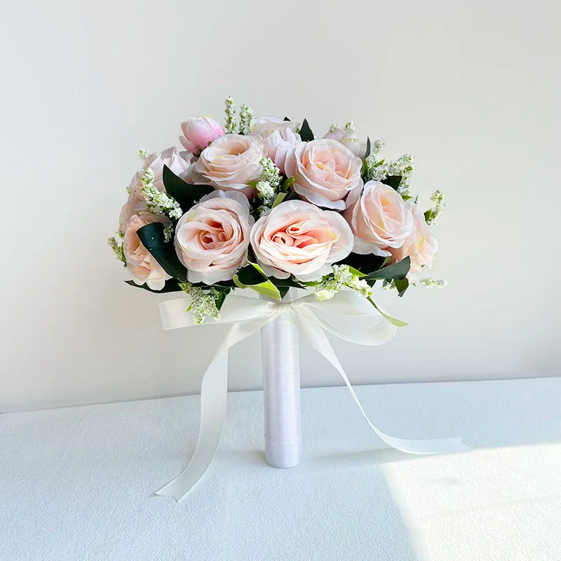 A bouquet of soft pink and blush roses with green foliage tied with a sheer white ribbon.