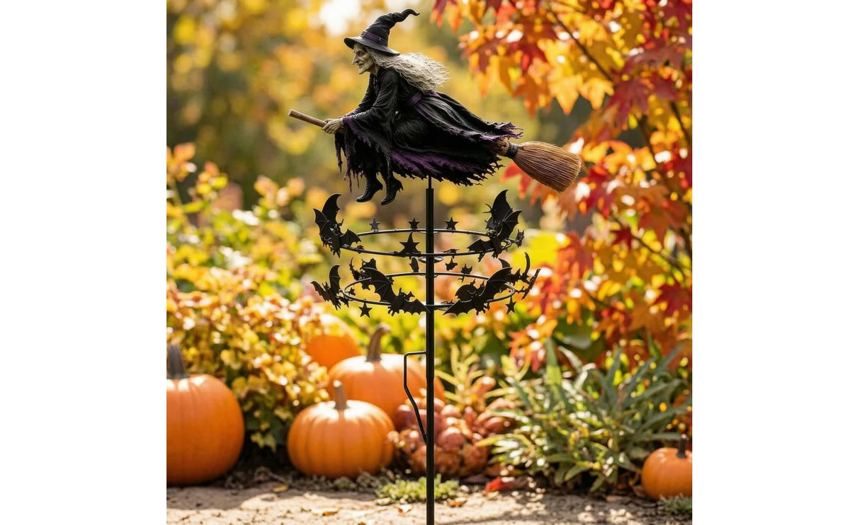A whimsical witch wind rotor garden decor featuring a black witch hat and feathered wings standing on a metal stake amidst au