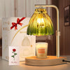 A brass adjustable candle warmer lamp with a green glass shade illuminates a scented candle on a wooden base.