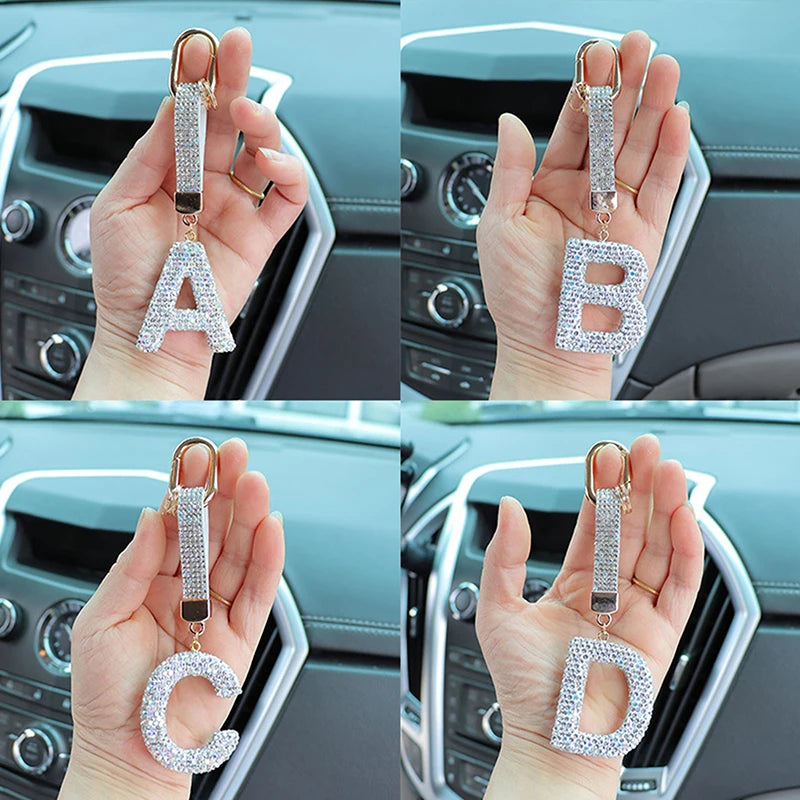 A set of crystal letter keychain charms A, B, and D held in a person's hand against a car interior background.