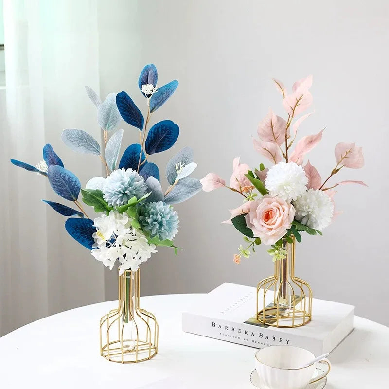 A golden iron hollow vase holds a floral arrangement featuring blue and pink foliage and white hydrangeas.