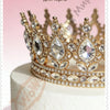 A gold crystal rhinestone crown cake topper displayed on a white cake.