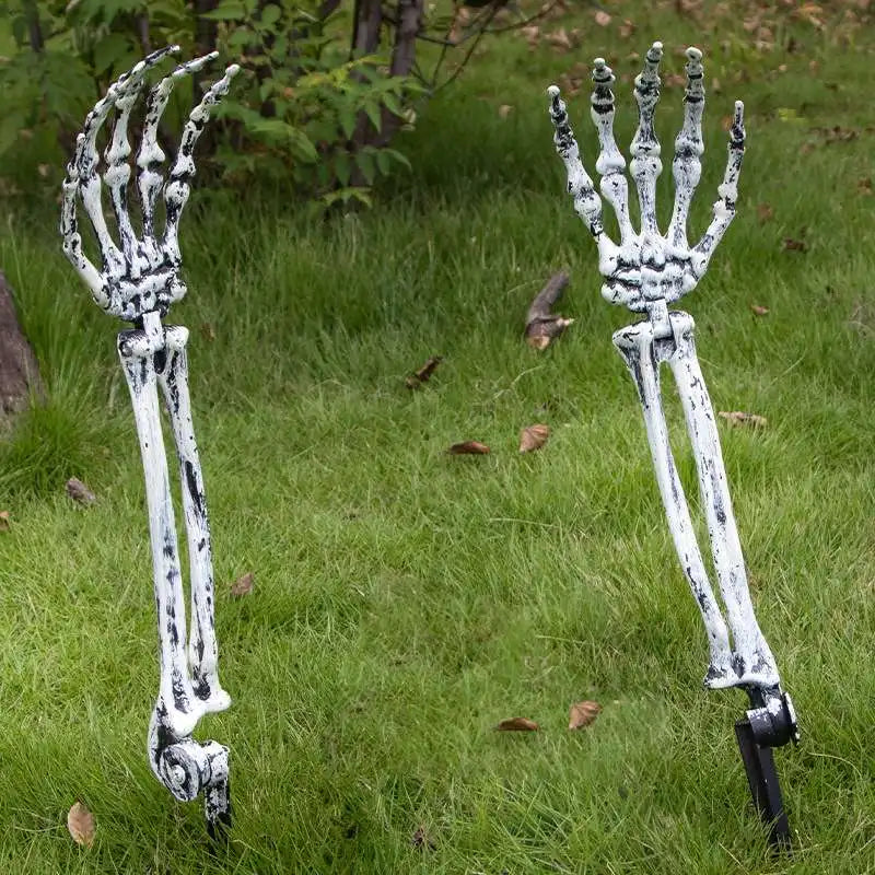 A pair of realistic white skeleton arm stakes used for Halloween lawn decor standing in green grass.
