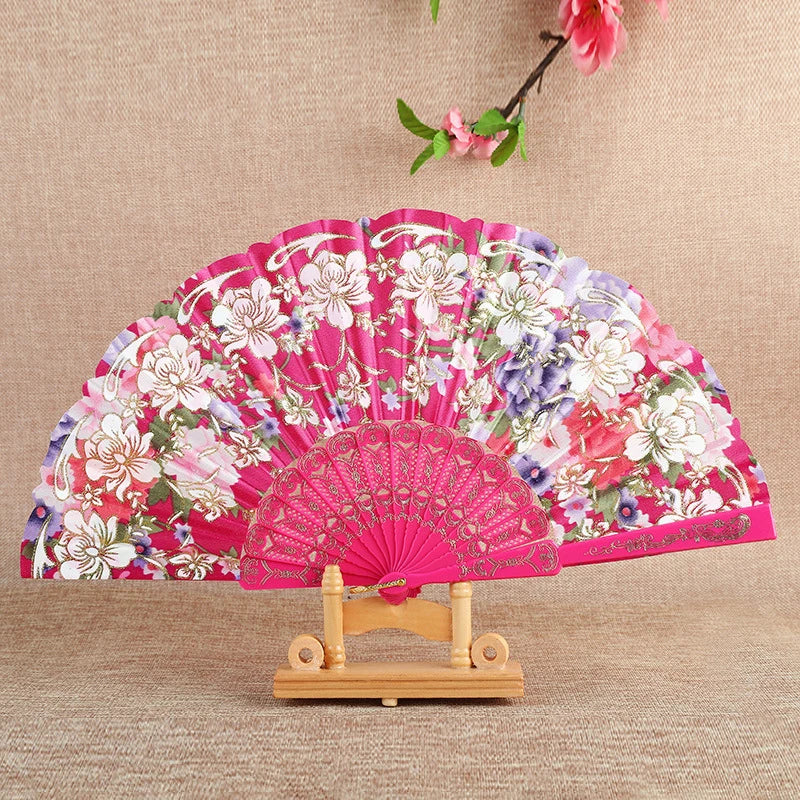 Pink floral silk folding fan displayed on a wooden stand with pink flowers hanging above.