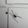 A black spider is affixed to a white refrigerator door, used as a realistic horror decor magnet.