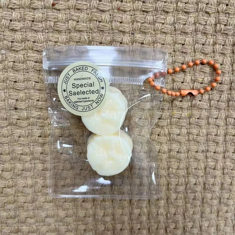 A clear plastic bag contains several small, pale yellow fruit-shaped keychains on a woven burlap background.