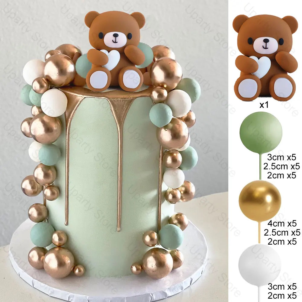 A tiered cake topper featuring a brown teddy bear and surrounding pink, gold, and mint green ball decorations.