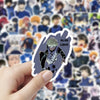 A hand holds a blue lock cartoon graffiti sticker featuring an anime character.
