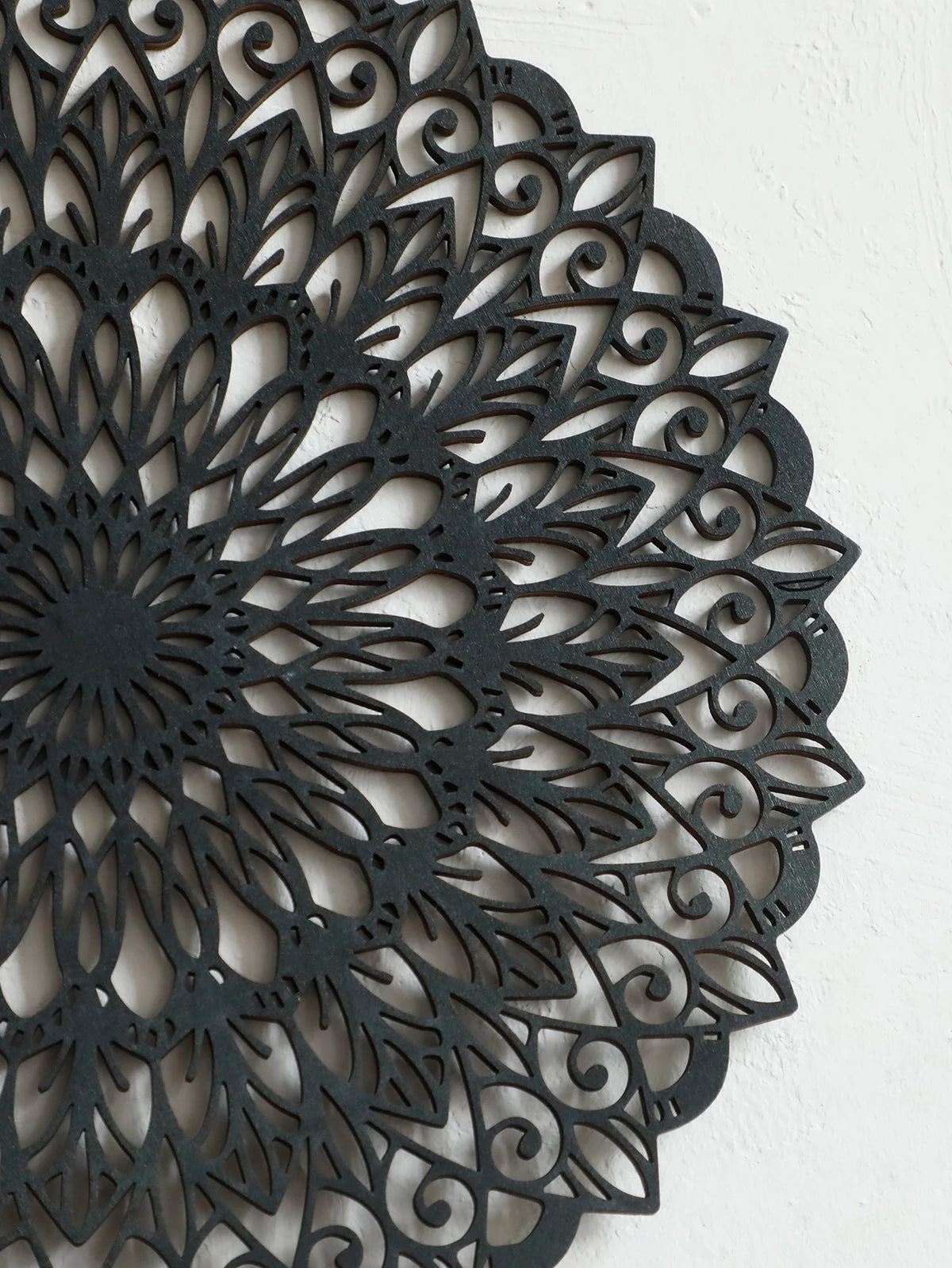 Decoración de pared de mandala de madera gris oscuro con intrincados patrones recortados.