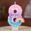 A large number eight candle decorated with iridescent glitter and a rainbow design.