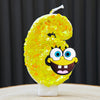 A yellow sponge cake candle shaped like the number 6, featuring a cartoon face design.