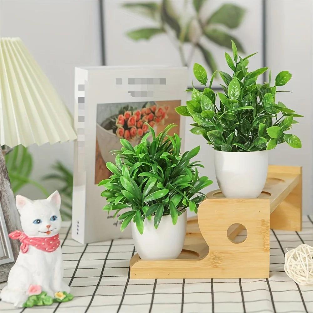 A set of four mini artificial bonsai plants in white pots displayed on a wooden stand with a white cat figurine.