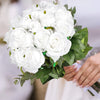 A bouquet of white artificial silk roses with green leaves being held by a person.