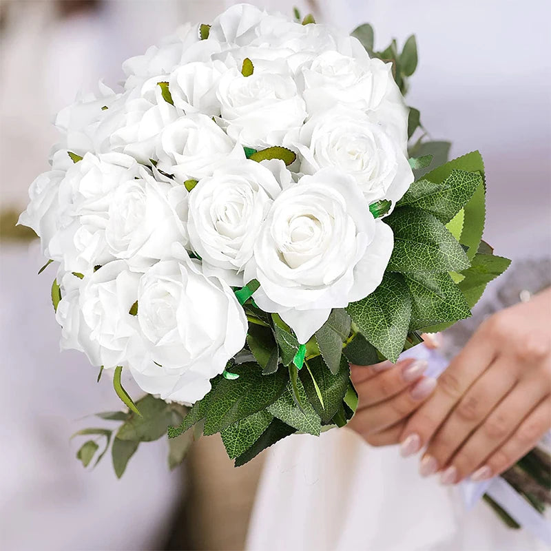 A bouquet of white artificial silk roses with green leaves being held by a person.