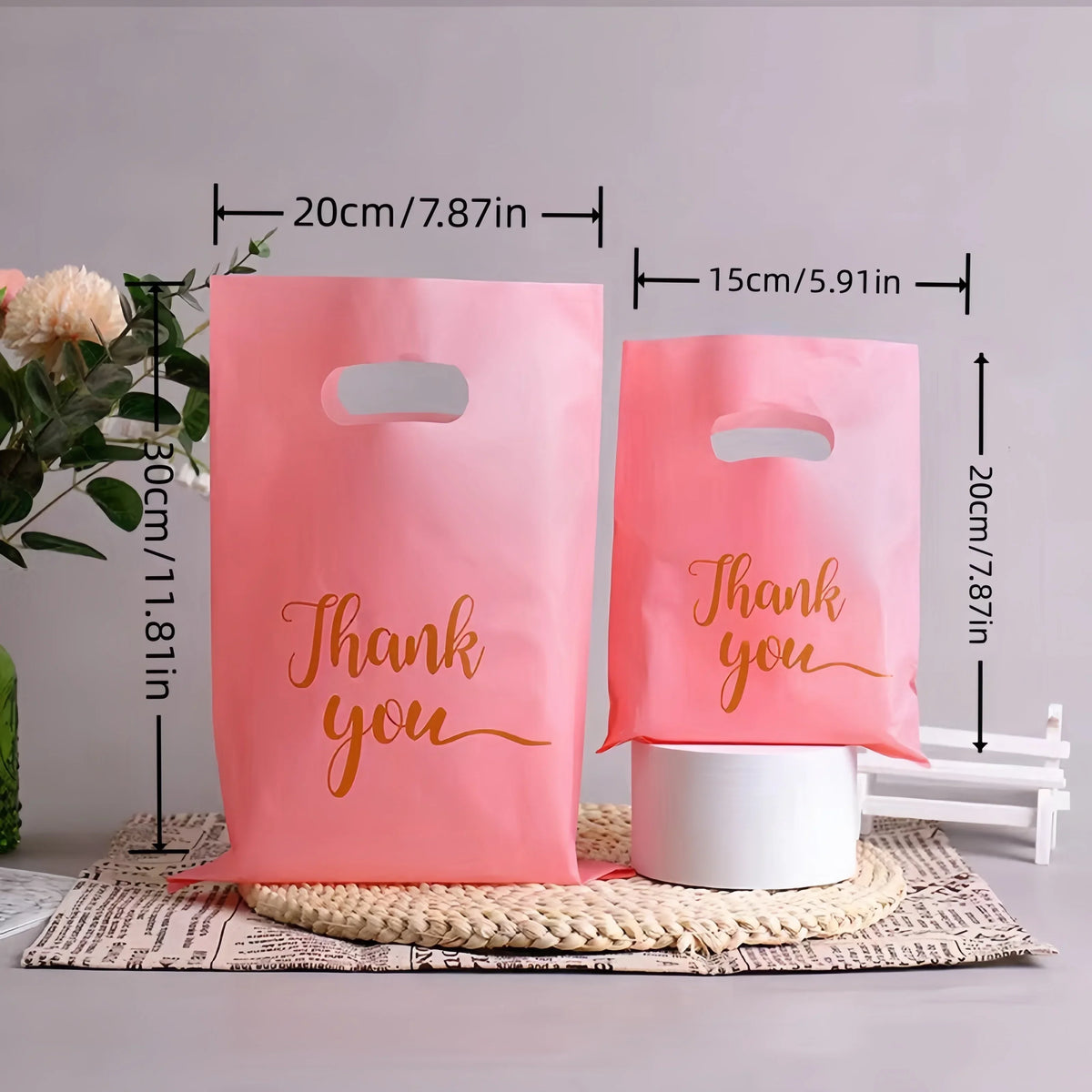 Pink paper gift bags with thank you message and handles displayed on a wooden surface.