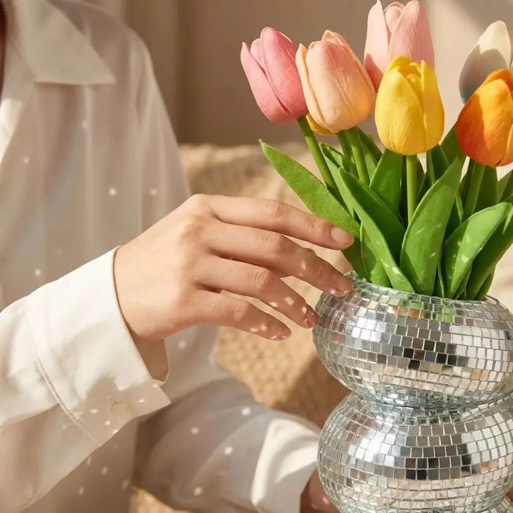 A hand places a bouquet of pink and yellow tulips into a silver disco ball spiral vase.