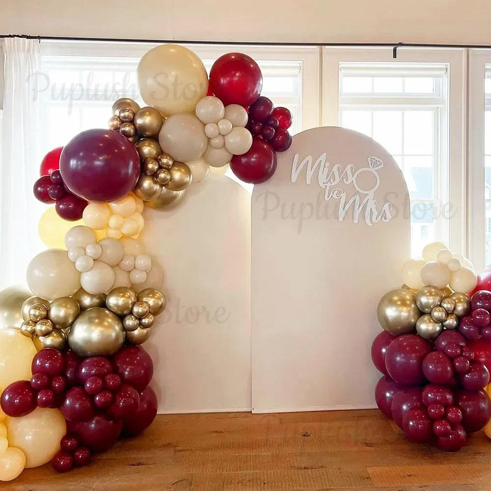 A display of deep burgundy and gold latex balloons arranged in a tiered, floral design against a white backdrop.