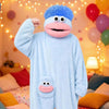 A light blue plush monster loungewear romper with a pink mouth and large eyes is displayed indoors.