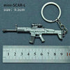 A silver miniature SCAR-L assault rifle model attached to a keyring, measured against a ruler.