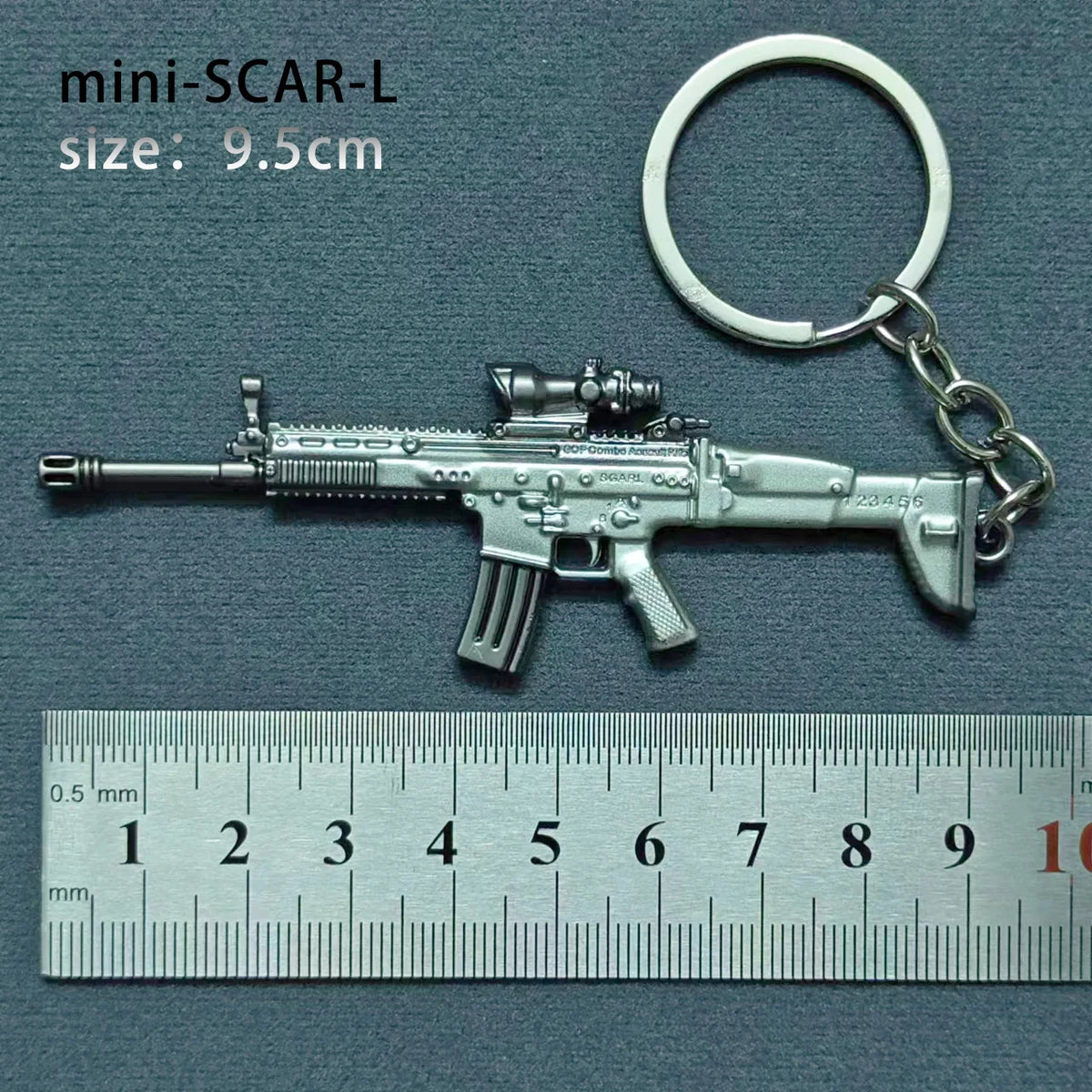 A silver miniature SCAR-L assault rifle model attached to a keyring, measured against a ruler.