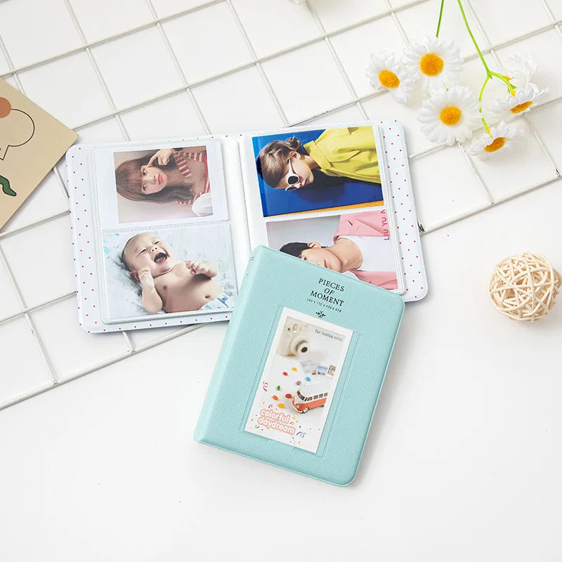 A teal photo album with six pockets displaying instant film photos of a baby and a person.