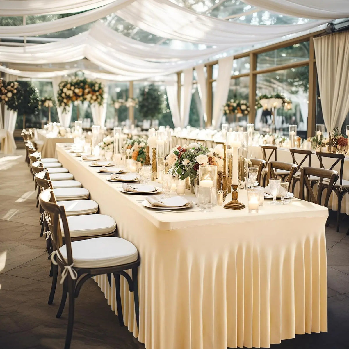A long table set for an event with white linens, gold accents, and floral arrangements under a draped canopy.
