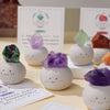 A collection of bean-shaped decorative stones in various shades of purple and green crystals displayed on a light surface.