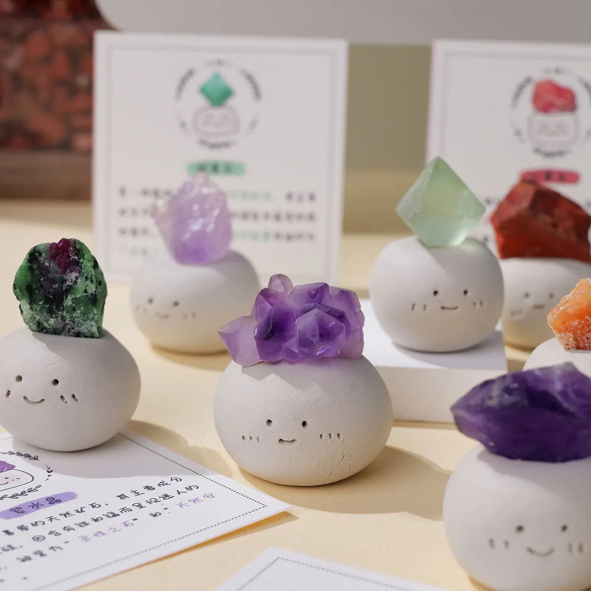 A collection of bean-shaped decorative stones in various shades of purple and green crystals displayed on a light surface.