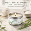 A jar of citronella scented candle sits on a light surface with a white towel and green leaves.