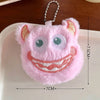 A pink fuzzy plush monster keychain with large eyes and a wide smile is displayed on a white surface.