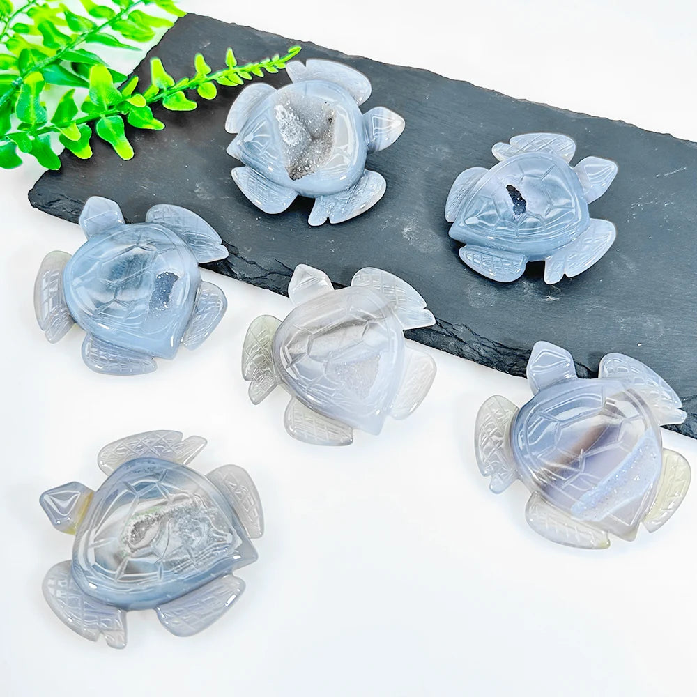 A set of natural blue-gray agate crystal figurines resting on a dark slate surface with green foliage.
