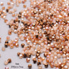 A close-up of mixed colored faceted bicone glass beads in shades of peach and amber scattered on a white surface.