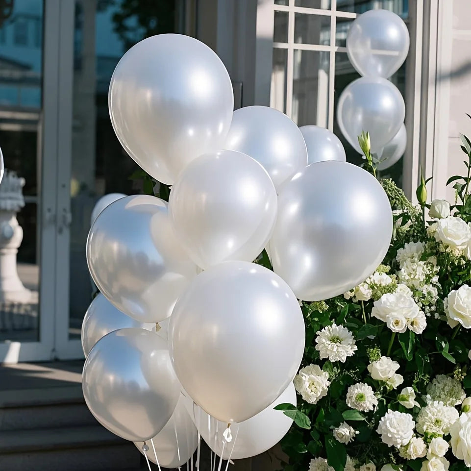A cluster of pearl white latex balloons arranged next to a bouquet of white flowers.